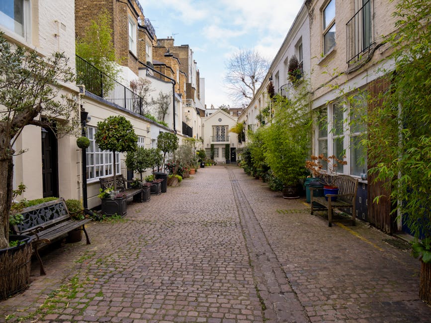 A white Victorian-style terraced house with intricate architectural details, including rounded bay windows and decorative cornices, set against a clear, vibrant blue sky. In front of the property, the